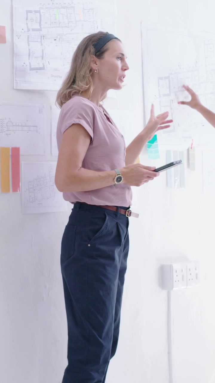 Video verticale: Designer di studio con top rosa che reagisce al braccio destro, usando un tablet per scegliere i colori.