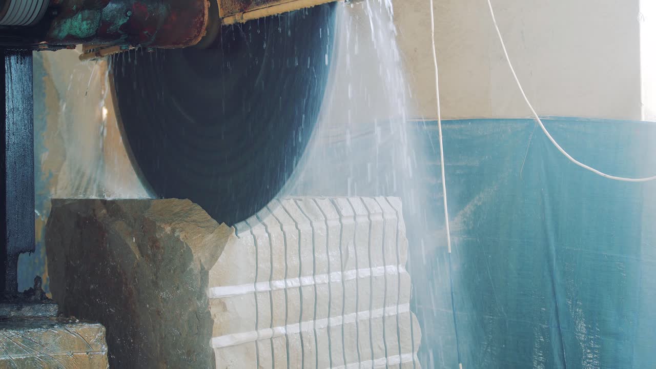Machine for cutting and sawing stone. A large circular electric saw spills a block of stone. Water drops