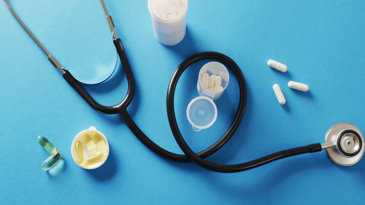 Video of stethoscope with pills and capsules on blue background with copy space