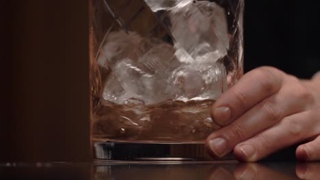 a bartender is pouring spirit and liquor into the stirring glass and start to stir along a lot of ice using a long copper bar spoon.