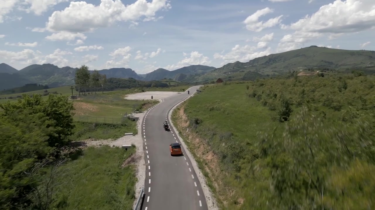 Vista aérea de un coche y motocicletas circulando por la pintoresca carretera Transalpina de Apuseni a través de exuberantes paisajes montañosos.