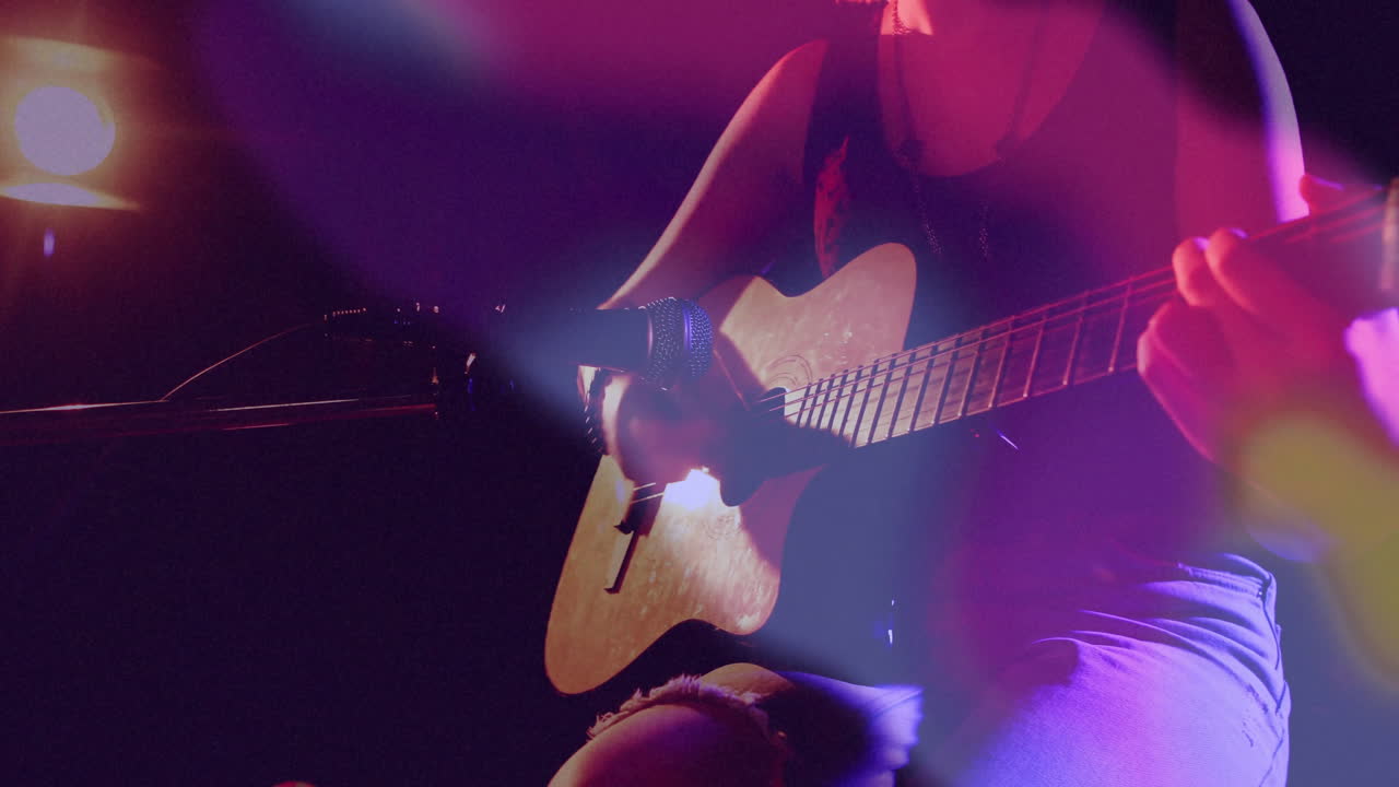 Female musician strumming guitar on dark stage, showing animated light beams and graphic overlays