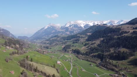 drone flight through a green swiss valley in the alps with snow and blue sky