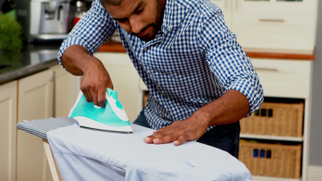 Mid section of man ironing clothes in kitchen 4k
