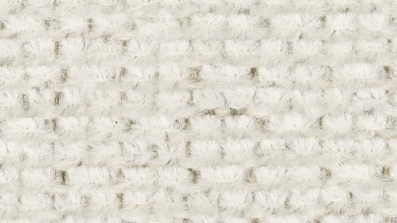 Macro shot slowly pans, revealing plush white carpet and subtle grey motif