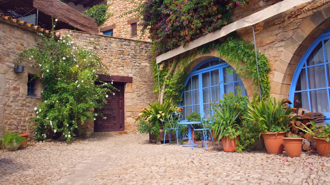 Splendida terrazza medievale colorata con piante, patio e grandi finestre blu, dall'atmosfera mediterranea