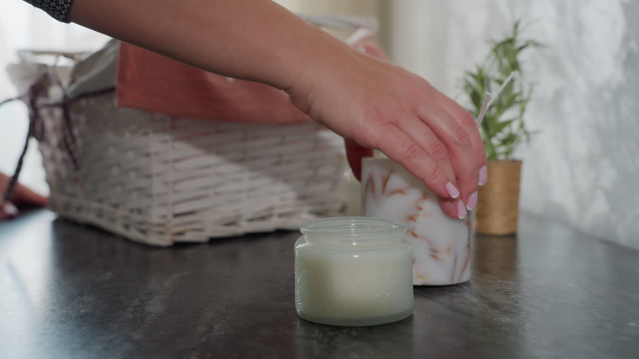Individual drops shopped item on marble table from basket covered with pink cloth beside small potted plant and decorative white candle