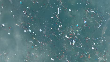 Top-down-panning-drone-shot-of-polluted-water-filled-with-plastic-trash-and-dead-coral-reef-in-the-turqouise-tropical-water-of-Balangan-Beach-Uluwatu-Bali-Indonesia