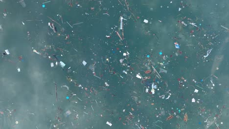 Top down panning drone shot of polluted water filled with plastic trash and dead coral reef in the turqouise tropical water of Balangan Beach Uluwatu Bali Indonesia