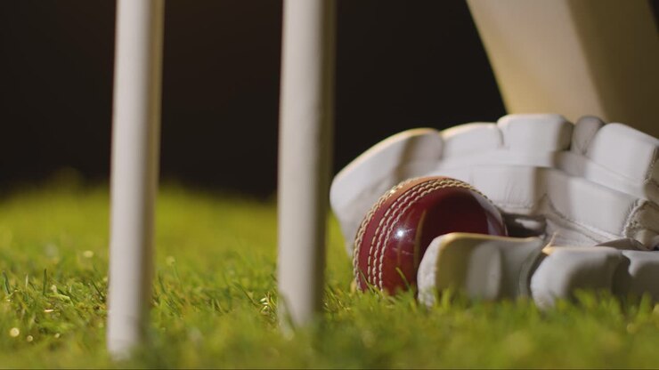 Natura morta di cricket con primo piano di mazza, palla e guanti sdraiati sull'erba dietro i paletti 1.