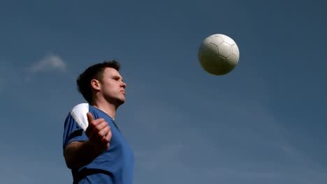 Football-Spieler-Mit-Der-Brust-Den-Ball-Unter-Blauem-Himmel