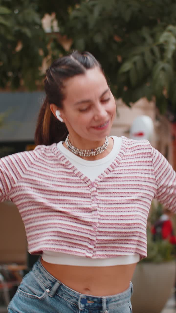 feliz mujer relajada de pie en la calle de la ciudad en auriculares inalámbricos escuchando música de baile al aire libre