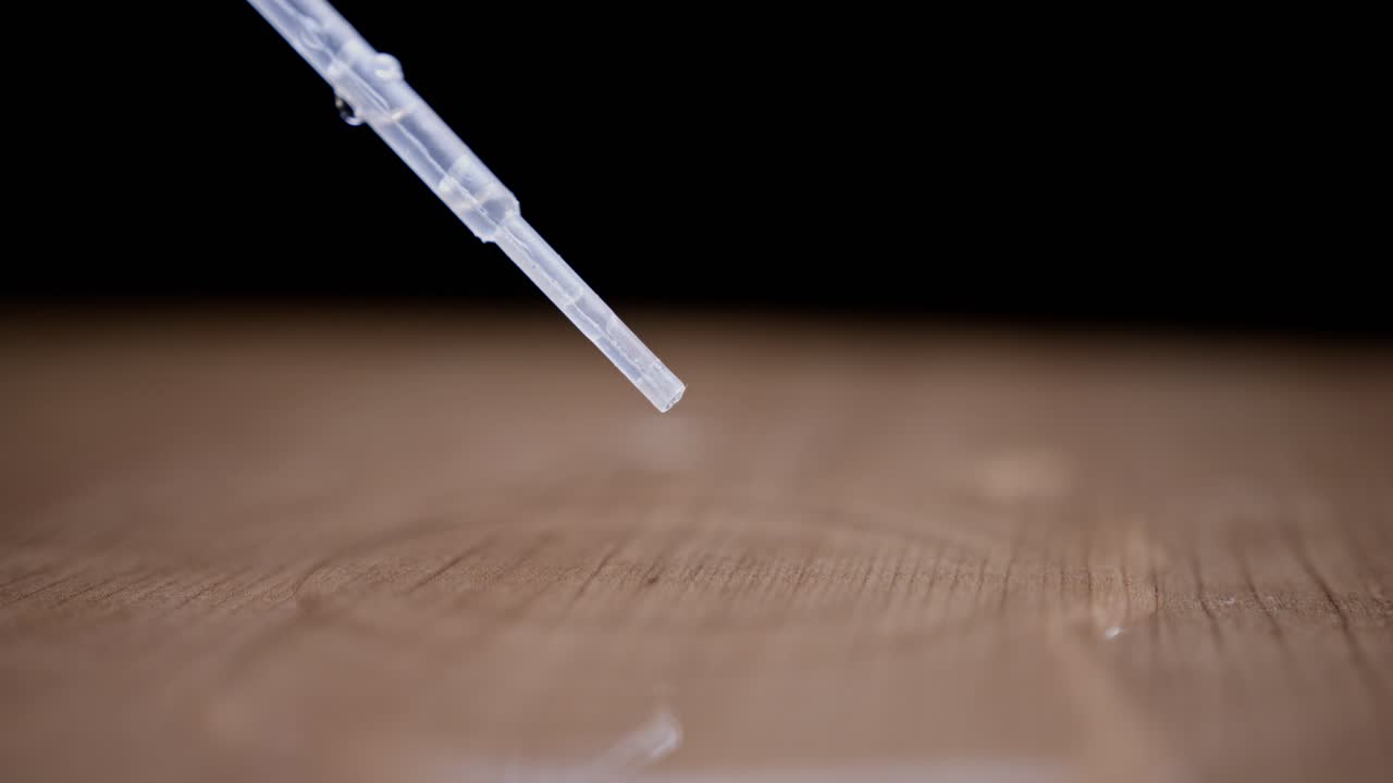 Water drop from a syringe falling onto a wooden surface in super slow motion