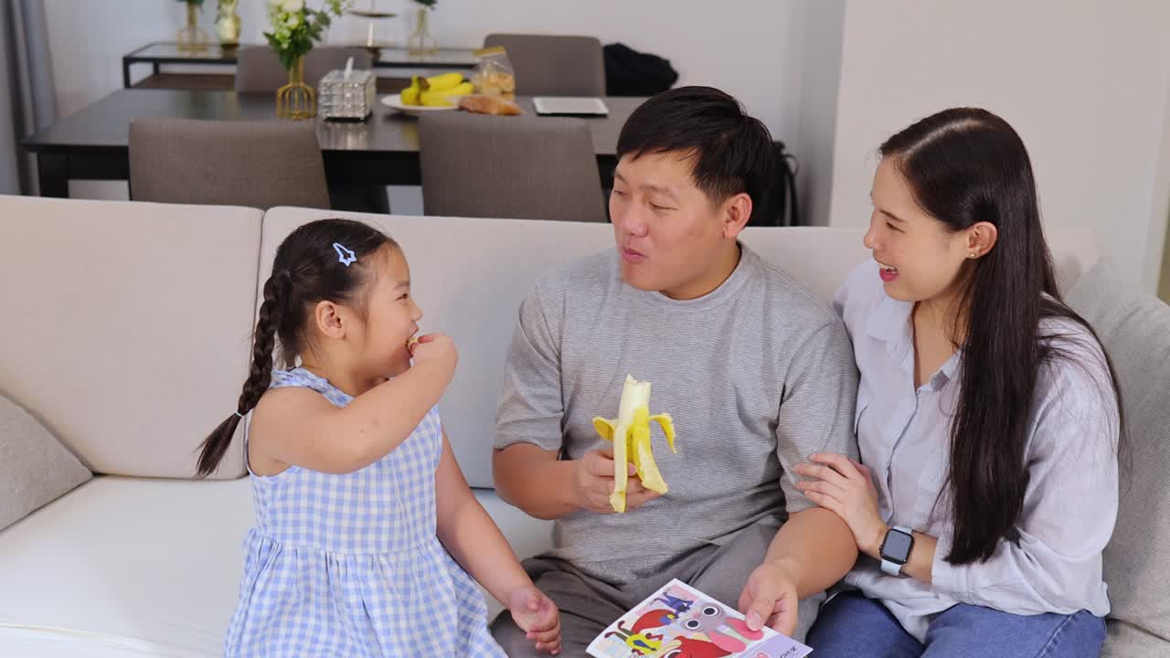 Happy Asian family eating a banana on the couch