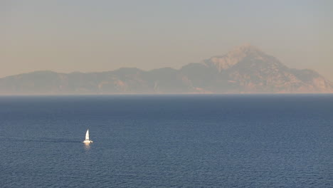 solitary sailboat on a calm sea with distant mountains