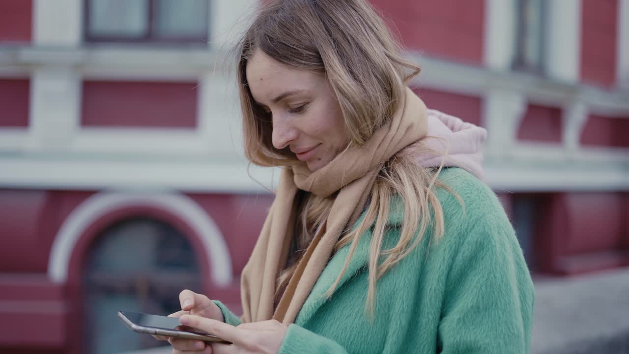 Donna che ascolta musica con gli auricolari e guarda lo smartphone per strada