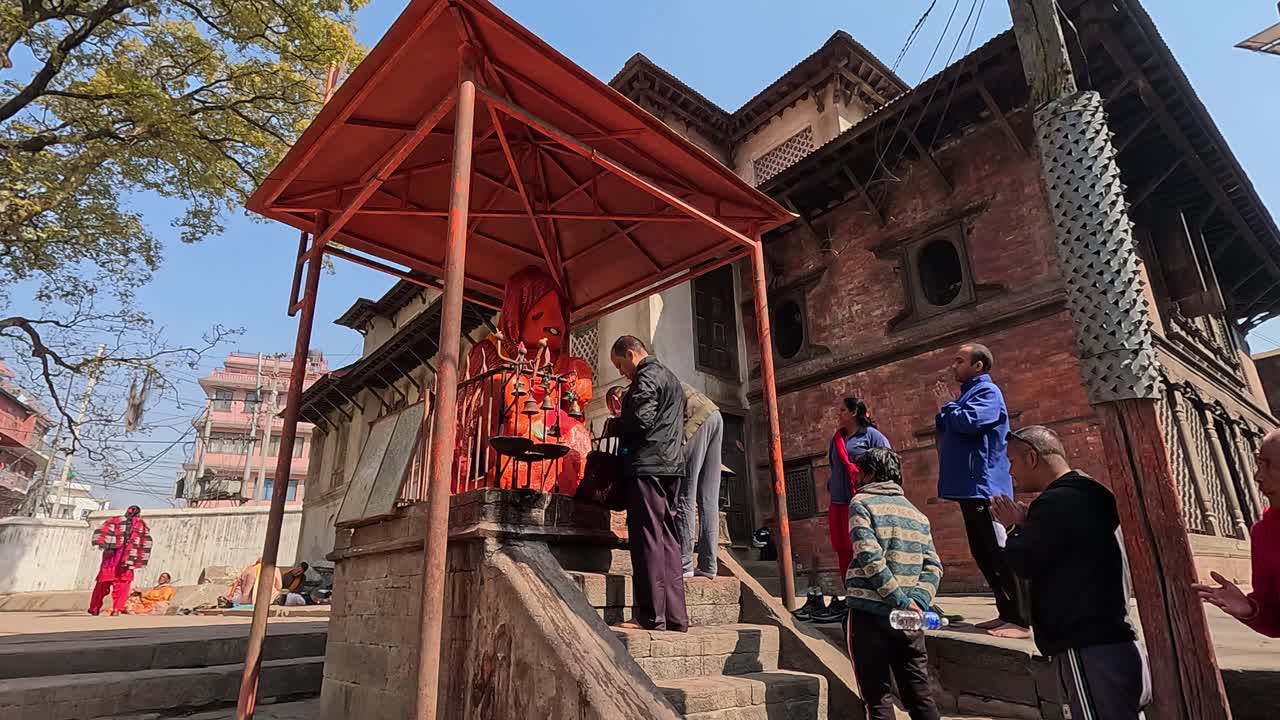 Faithful devotees gather to pray at the Gauri Temple pashupatinath, Kathmandu.  decorating the Hanuman statue covered in vibrant orange. A scene filled with spiritual devotion