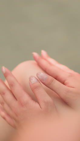 vista parcial de una mujer sentada al aire libre en un banco de madera con las piernas cruzadas, tocando suavemente la rodilla con las manos, el sujeto está suavemente iluminado por la luz solar, con un fondo borroso
