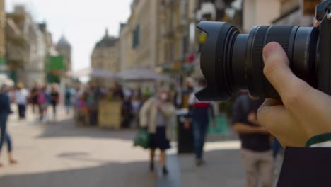 close up shot of man using focus ring on camera in busy street