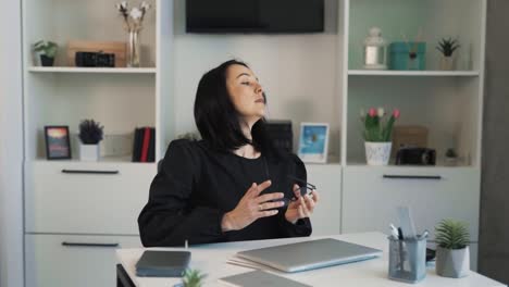 The-dark-haired-woman-is-sitting-at-a-desk-in-an-office,-having-finished-her-work-on-the-laptop