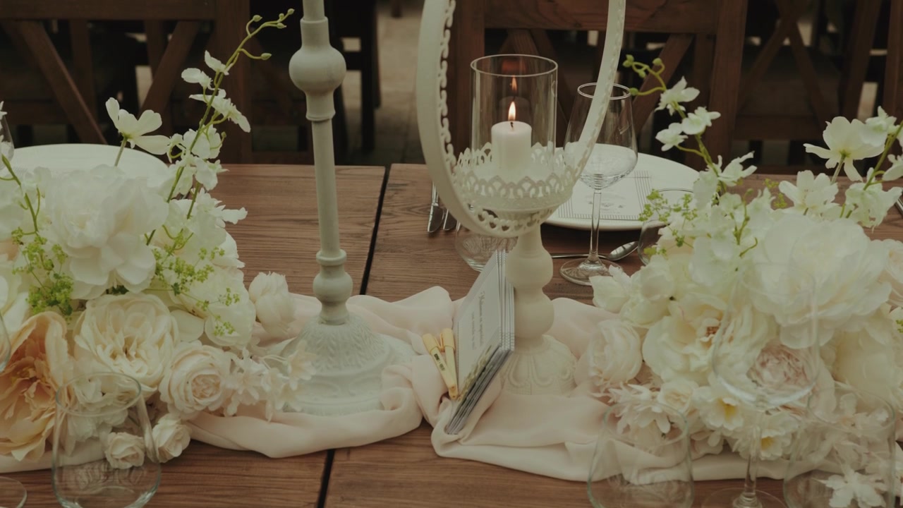 Close-up of an elegant wedding reception table decorated with luxurious white floral arrangements, candles, crystal glassware, and sophisticated table styling.