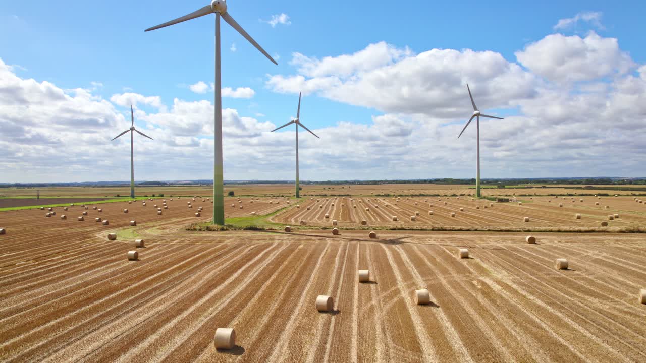 High above, the camera records the tranquil scene of wind turbines spinning gracefully in a Lincolnshire farmer's field, recently harvested and adorned with golden hay bales