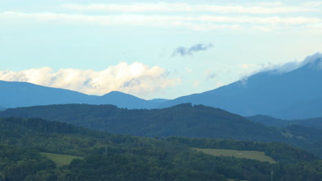 side slide a mountain top and white clouds moving over a mountainous landscape full of hills during a sunny day low clouds moving over the hills