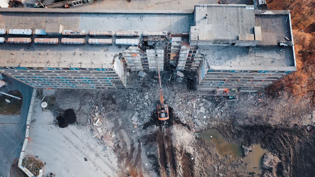 A demolition excavator destroys an old unusable building. Destruction of walls and concrete blocks. Aerial view