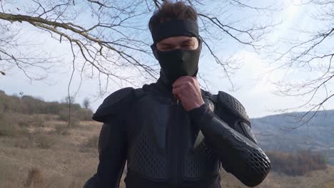 a mysterious ninja warrior in black armor adjusts his mask in a rural setting. perfect for action, martial arts, samurai, video games, and cinematic projects