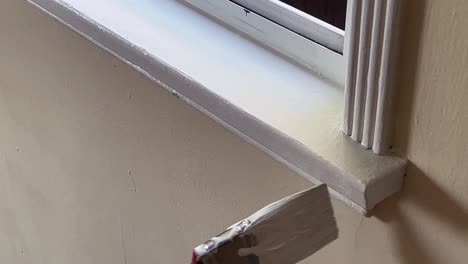 paint brush applying white paint to window trim, open window, close up on brush and hand