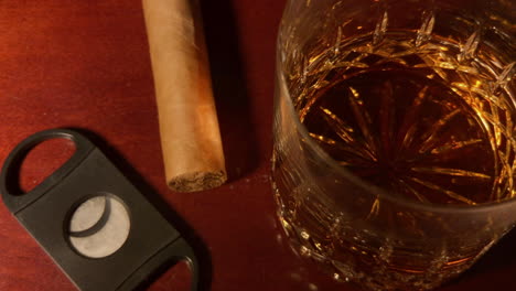 whiskey glass, cigar and cigar cutter sit on mahogany bar top