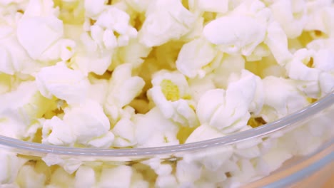 Macro-shot-of-popcorn-in-transparent-glass-bowl-rotating-on-orange-surface,-close-up-view-in-4k