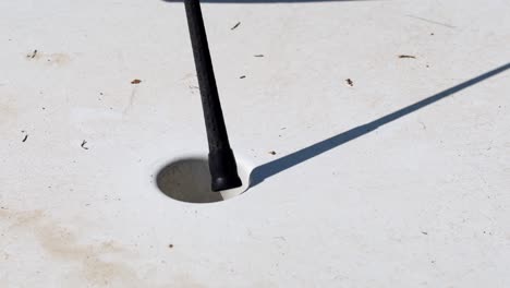 primer plano de un jugador de golf en miniatura pone la pelota dentro del agujero y la recoge, día