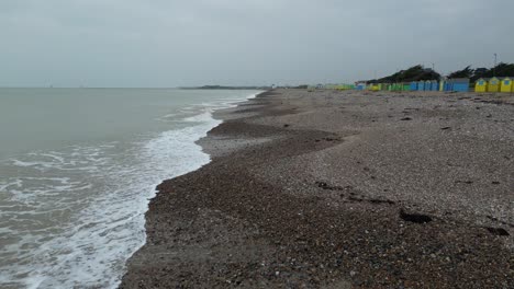 a tranquil, overcast day on a uk beach. gentle waves meet the shingle shore lined with colorful beach huts. serene coastal scene.