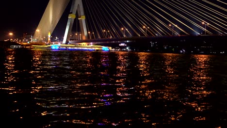 un barco de recreo navega a lo largo del río bajo el puente de cables