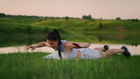 Woman-stretches-her-back-and-makes-bends-lying-on-the-grass-girl-trains-in-the-city-park-in-nature.