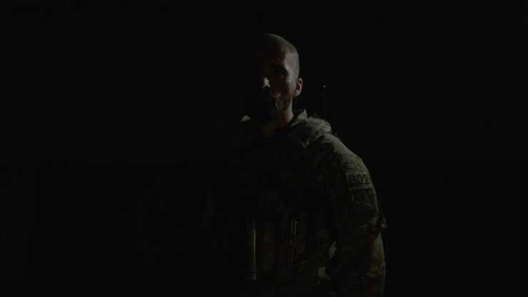 Front view of man with scratches on his face holding shotgun, posing for camera in a dark room with flickering red light after playing airsoft