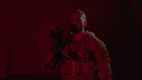 Front-view-of-man-with-scratches-on-his-face-holding-shotgun,-posing-for-camera-in-a-dark-room-with-flickering-red-light-after-playing-airsoft