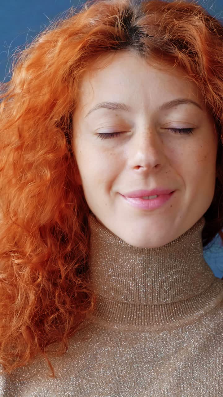 Smiling woman with curly red hair wearing a cozy turtleneck sweater, showcasing warmth and approachability in a bright indoor setting with soft lighting