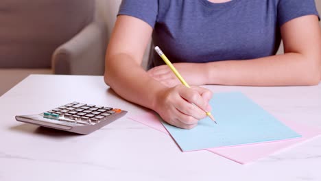 woman is using a calculator to calculate and write down her monthly accounting expenses at home