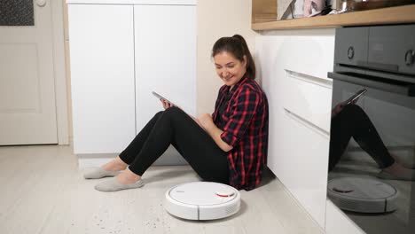 woman with phone looking at robot vacuum cleaner on floor