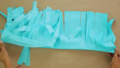 hands organizing strips of light blue tissue paper for diy project on flat surface