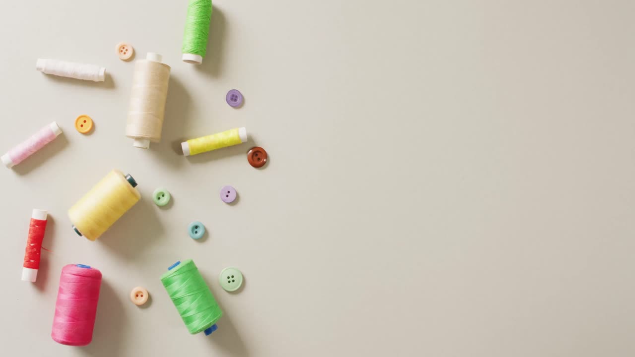 Video of coloured sewing threads and buttons on grey background with copy space