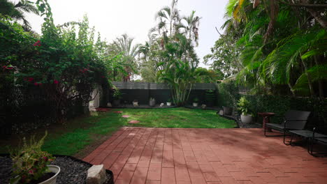 lush green small grass backyard lined with rock garden and black chairs seating in shade