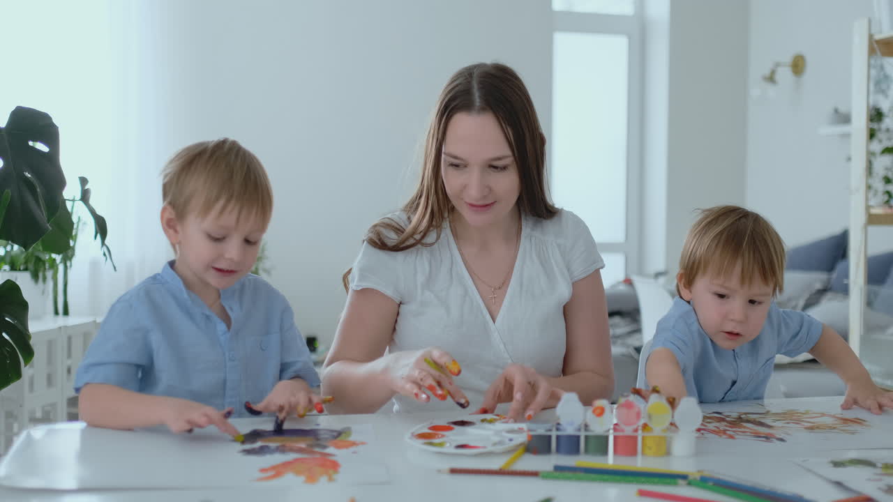 la familia se divierte pintando en el papel con los dedos en la pintura. mamá y dos niños pintan con los dedos en el papel