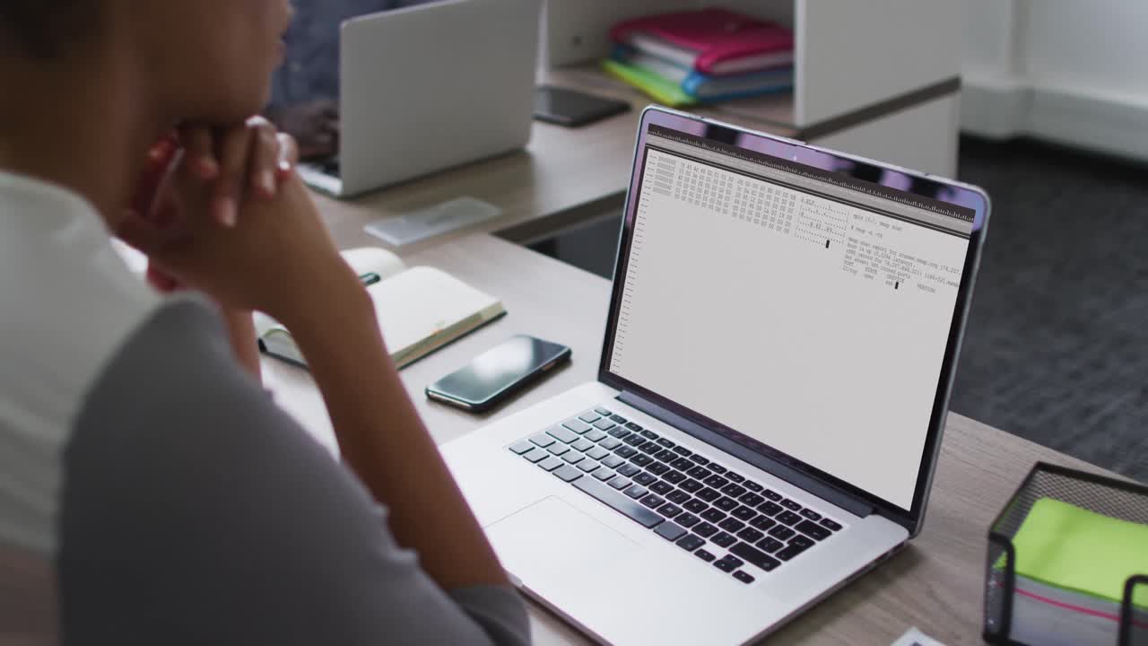 Mixed race woman sitting at desk watching coding data processing on laptop screen