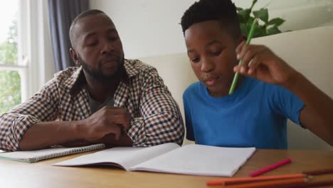 happy african american father sitting at kitchen table helping son with school work