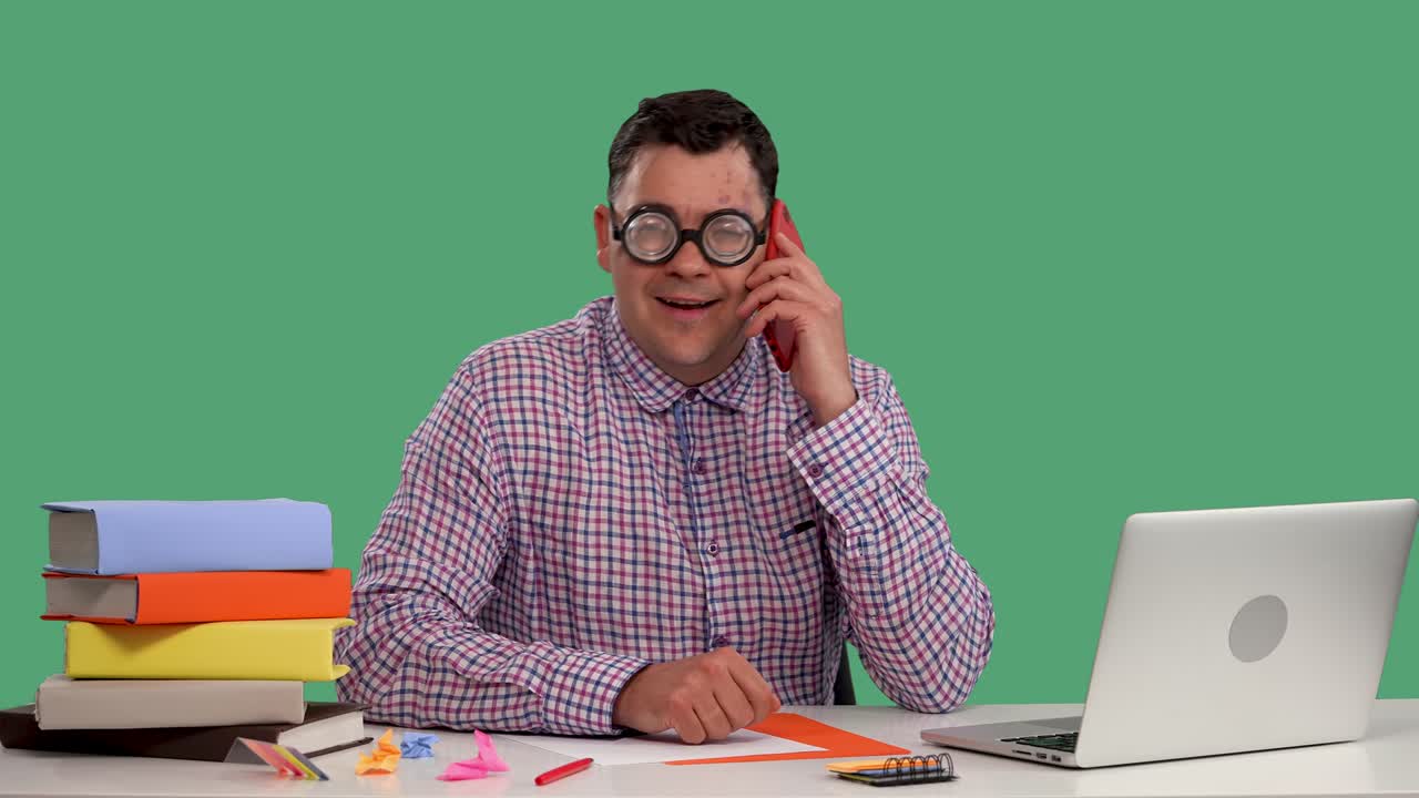 A man sits at a table in front of an open laptop and talks on a cell phone. Portrait of a man in the studio on a green screen. Slow motion. Close up