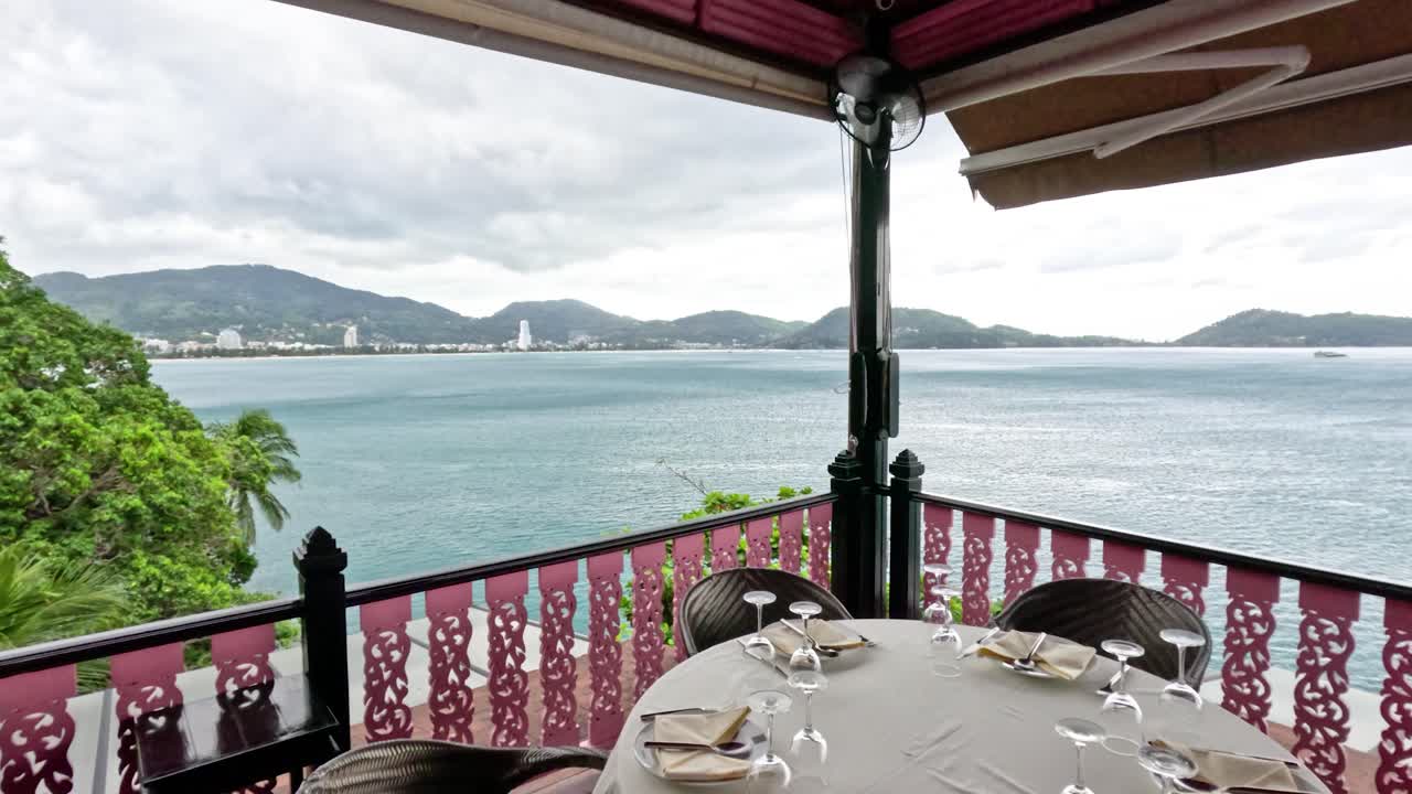 Camera pans from lush greenery to ocean view, elegant dining table, overcast daylight, tranquil mood