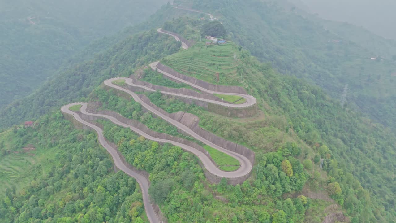 A serpentine road curves gracefully through vibrant green mountains, offering a breathtaking view of natural beauty and human engineering in harmony, captured from a high-altitude aerial perspective.